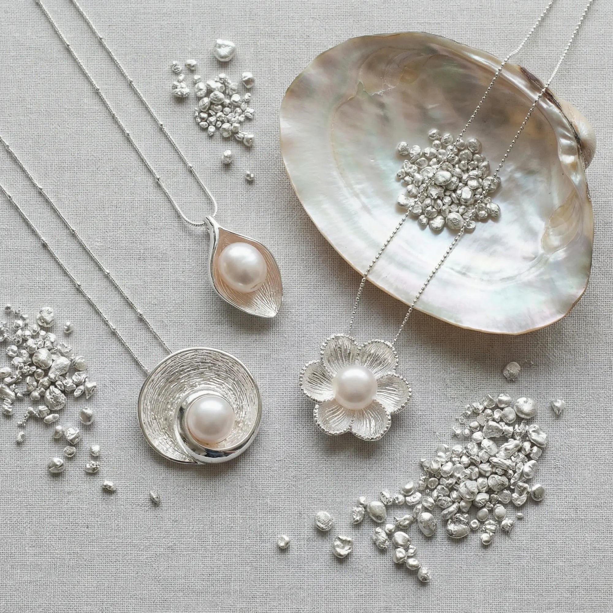 Three unique fresh water pearl necklaces featuring flower and leaf designs displayed with raw 925 silver grains and an iridescent mother of pearl shell.