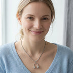 Woman wearing silver DJ headphone pendant necklace on thick box chain with V-neck blue sweater, neutral background