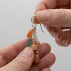 Hands gently holding the comfortable 925 sterling silver leaf chain drop earrings to show the tactile matte peach natural stones.