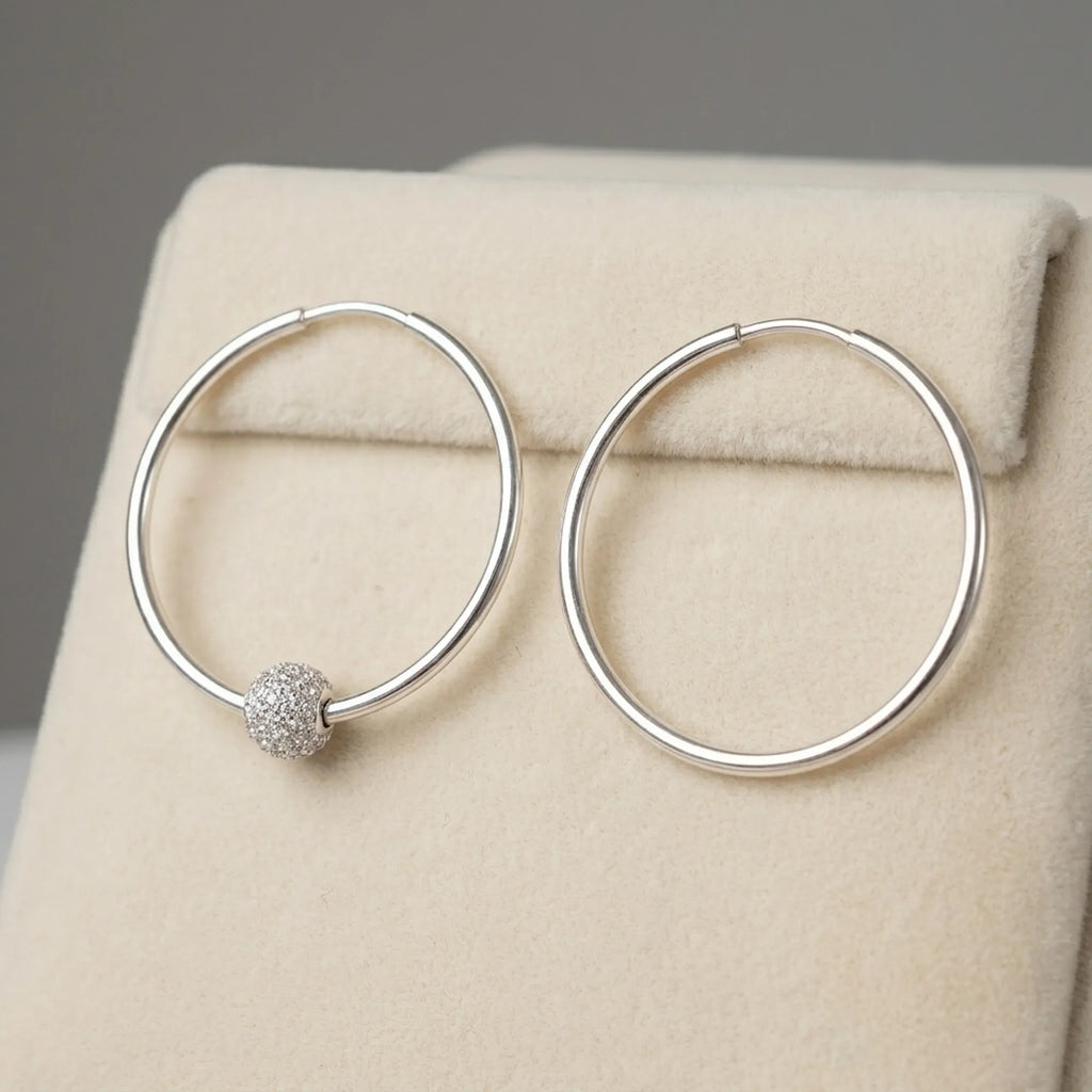 Silver hoop earrings on cream velvet display stand one showing CZ pave bead position and one showing clean hoop without bead