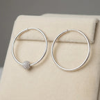 Silver hoop earrings on cream velvet display stand one showing CZ pave bead position and one showing clean hoop without bead