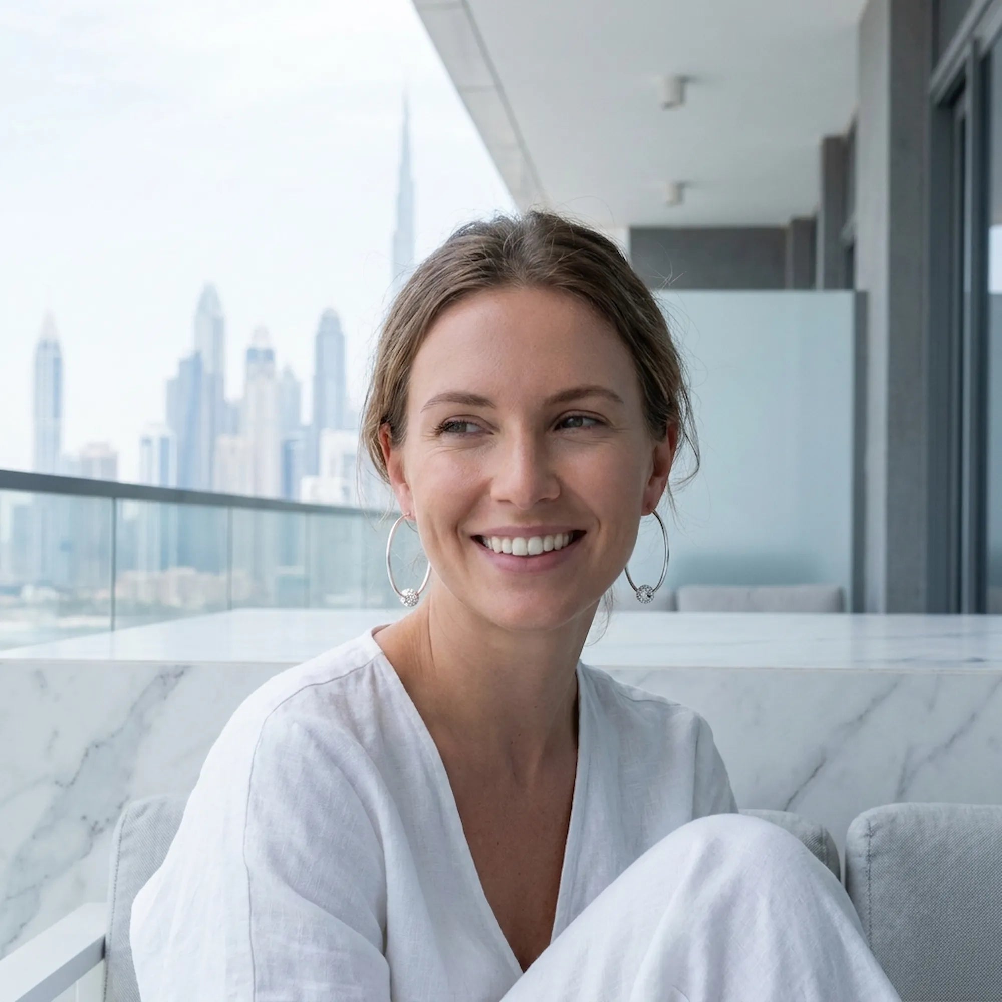 Woman wearing 2-in-1 silver hoop earrings with CZ bead on balcony with Burj Khalifa and Downtown Dubai skyline behind
