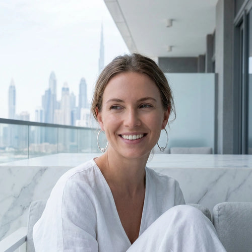 Woman wearing 2-in-1 silver hoop earrings with CZ bead on balcony with Burj Khalifa and Downtown Dubai in skyline behind.