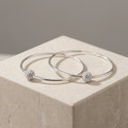Pair of silver 2-in-1 hoop earrings with CZ pave bead overlapping on cream stone cube neutral taupe background