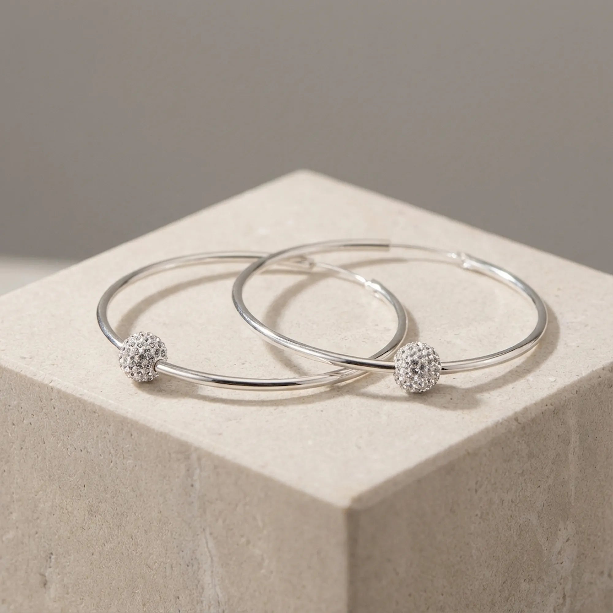 Pair of silver 2-in-1 hoop earrings with CZ pave bead overlapping on cream stone cube neutral taupe background