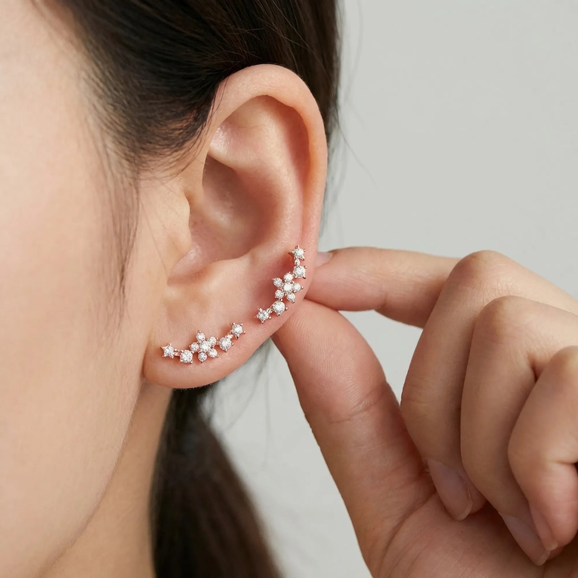 Close up of a woman easily adjusting the stackable rose gold ear cuff, demonstrating how it sweeps securely up the ear.