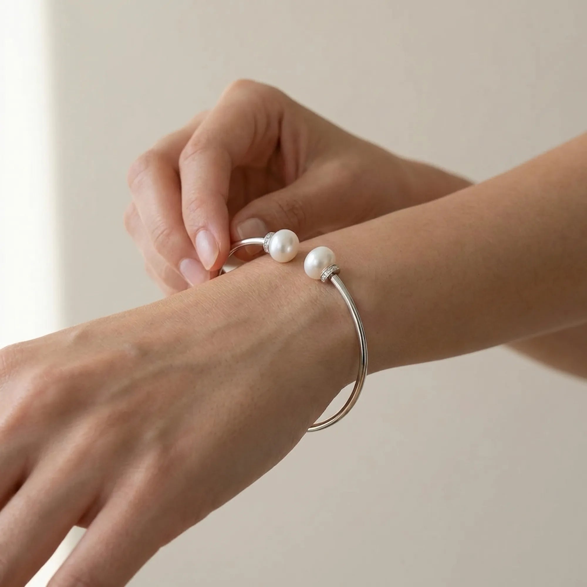 Close-up of a woman's hands gently adjusting the 925 sterling silver open-cuff pearl bangle on her wrist for a comfortable, secure fit.