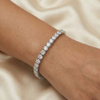 Close-up of a shimmering white cubic zirconia tennis bracelet worn on a wrist against a neutral cream silk fabric background