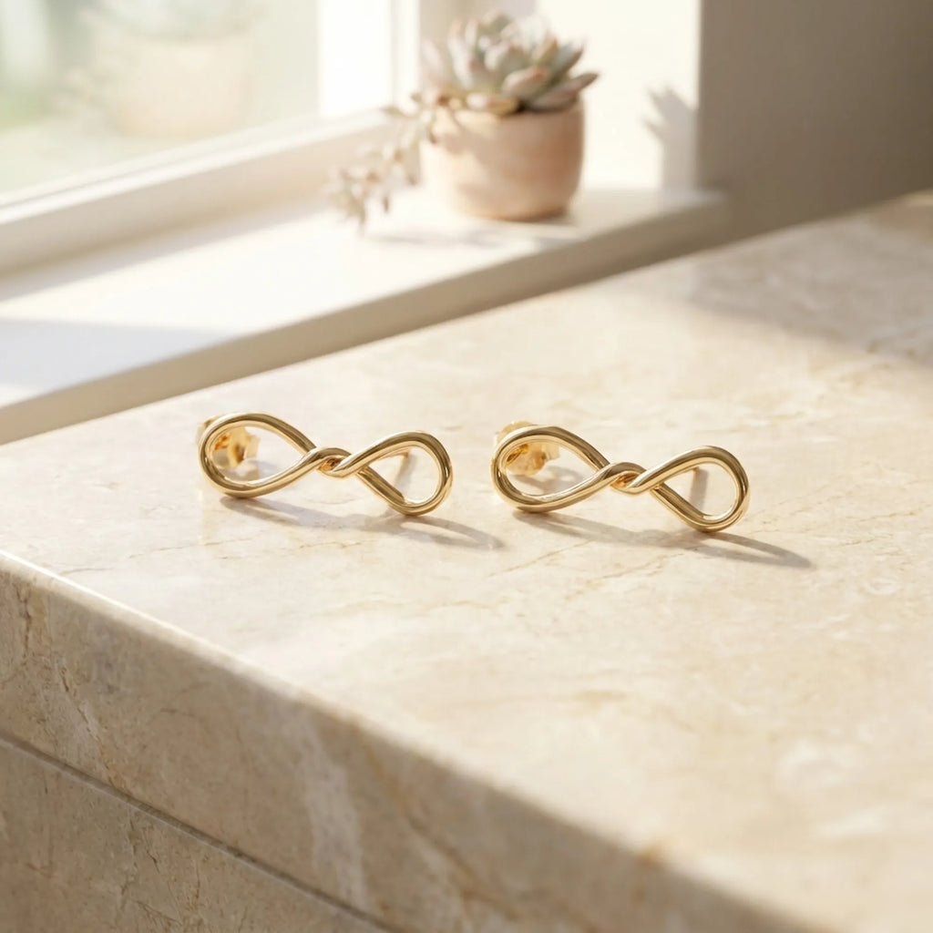Both gold infinity drop earrings laid flat on marble windowsill with succulent plant in background