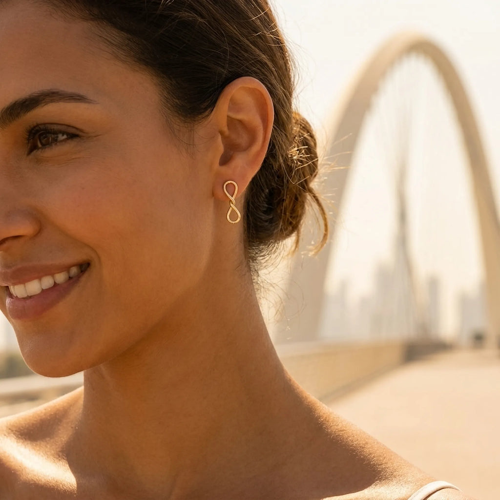 Model wearing gold infinity drop earrings, Dubai Infinity Bridge over Dubai Creek in background