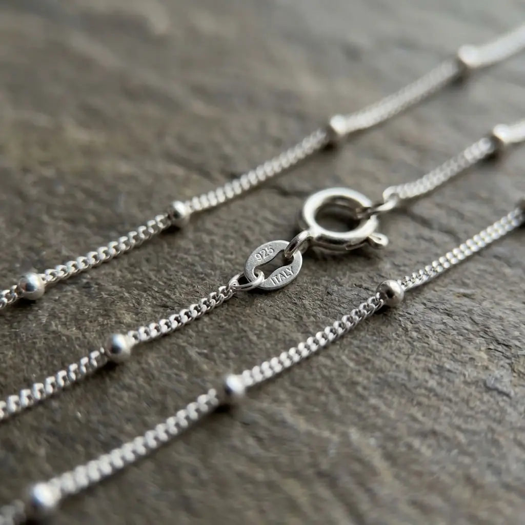 Close-up of silver station chain with polished bead accents, spring-ring clasp and visible 925 and ITALY markings on an end tag.