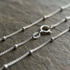 Close-up of silver station chain with polished bead accents, spring-ring clasp and visible 925 and ITALY markings on an end tag.
