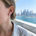 Jasmine bloom silver stud earring worn on ear — Dubai Marina skyline and waterfront in background, rhodium 925 silver