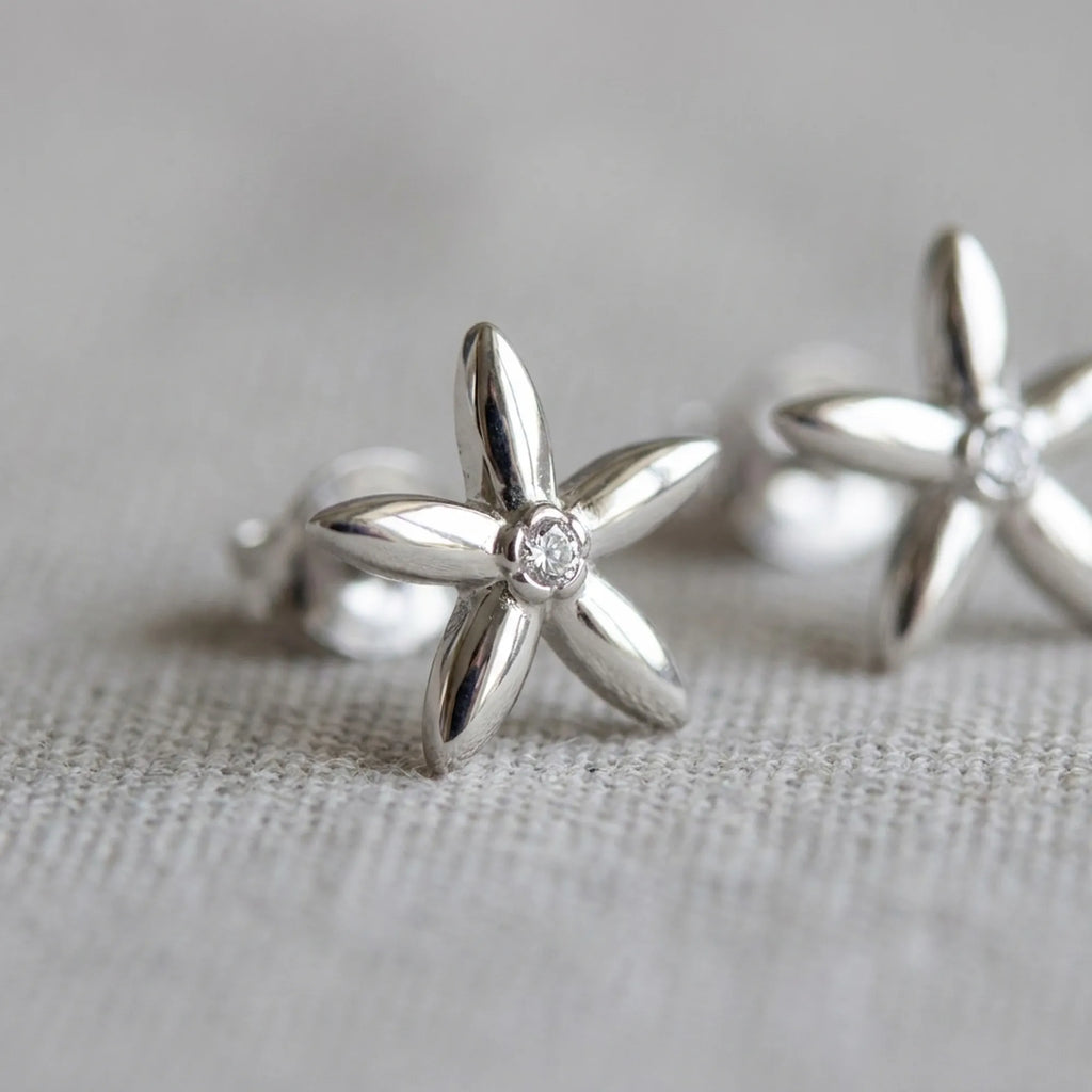 Close-up of jasmine flower stud earrings on linen — five-petal rhodium silver design with bezel-set CZ centre