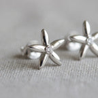 Close-up of jasmine flower stud earrings on linen — five-petal rhodium silver design with bezel-set CZ centre