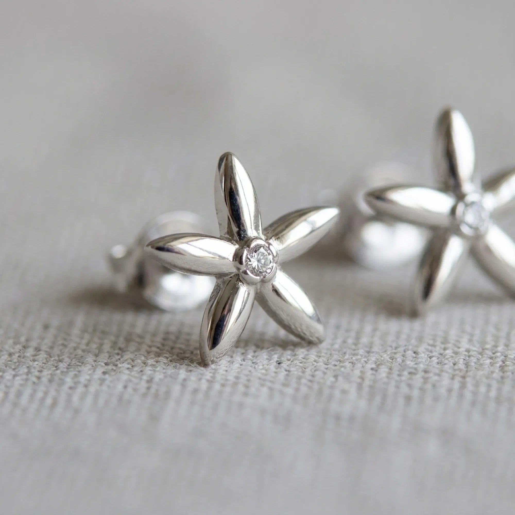 Close-up of jasmine flower stud earrings on linen — five-petal rhodium silver design with bezel-set CZ centre