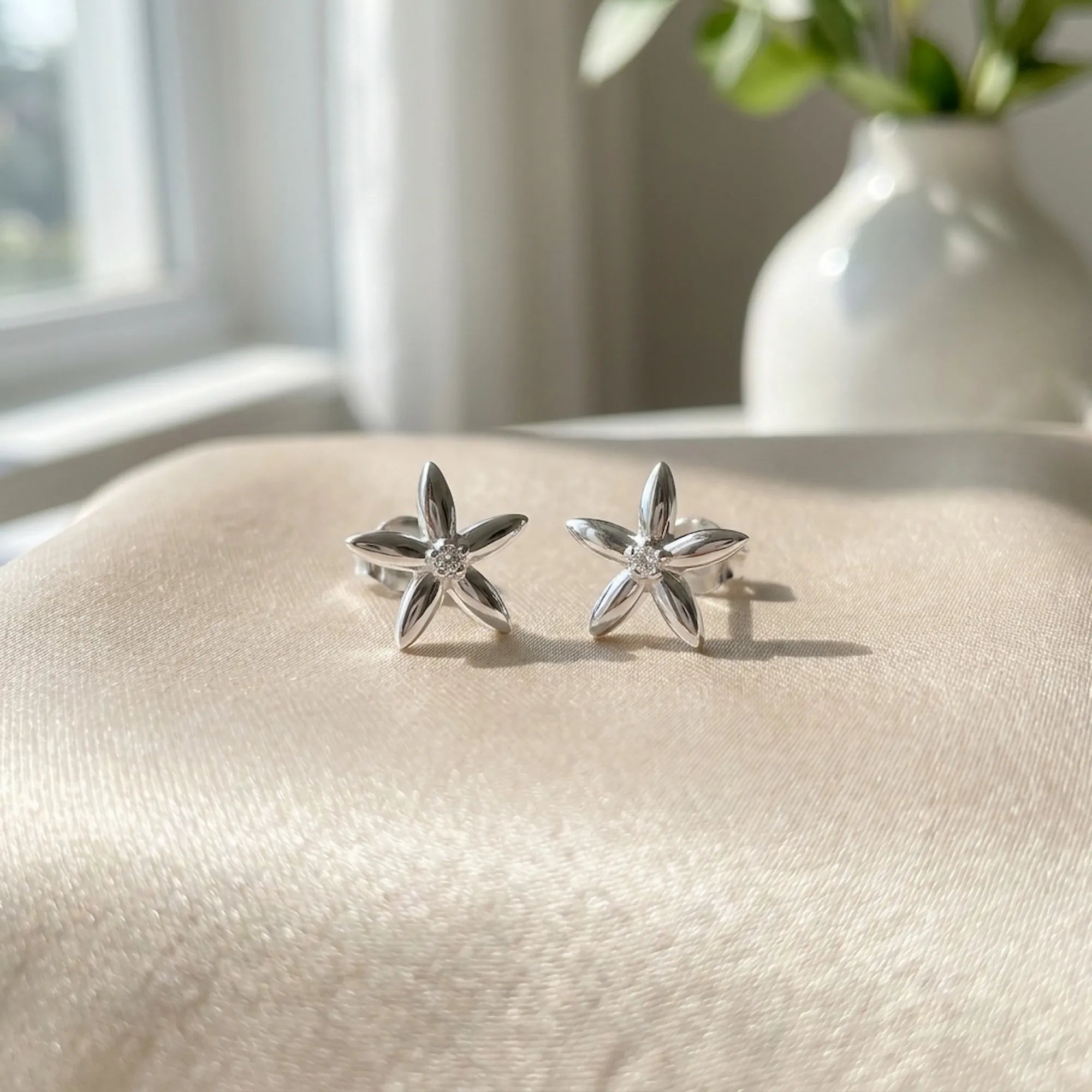 Jasmine silver stud earrings on cream satin fabric with plant vase — rhodium-plated 925 sterling silver, natural light