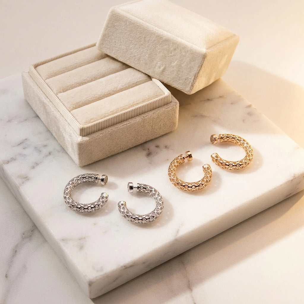 Silver and gold plated lattice hoop earrings with cubic zirconia displayed on marble next to a jewelry box in Dubai.