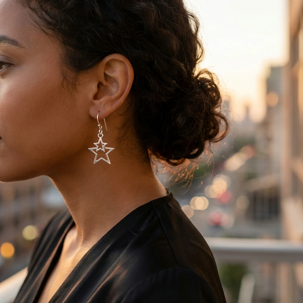Woman wearing pure-silver plated double star drop earrings outdoors in Dubai with a blurred city sunset background.