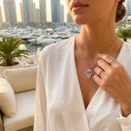 Woman wearing a necklace with a Hamsa pendant in an outdoor Dubai Marina setting with boats and buildings in the background.