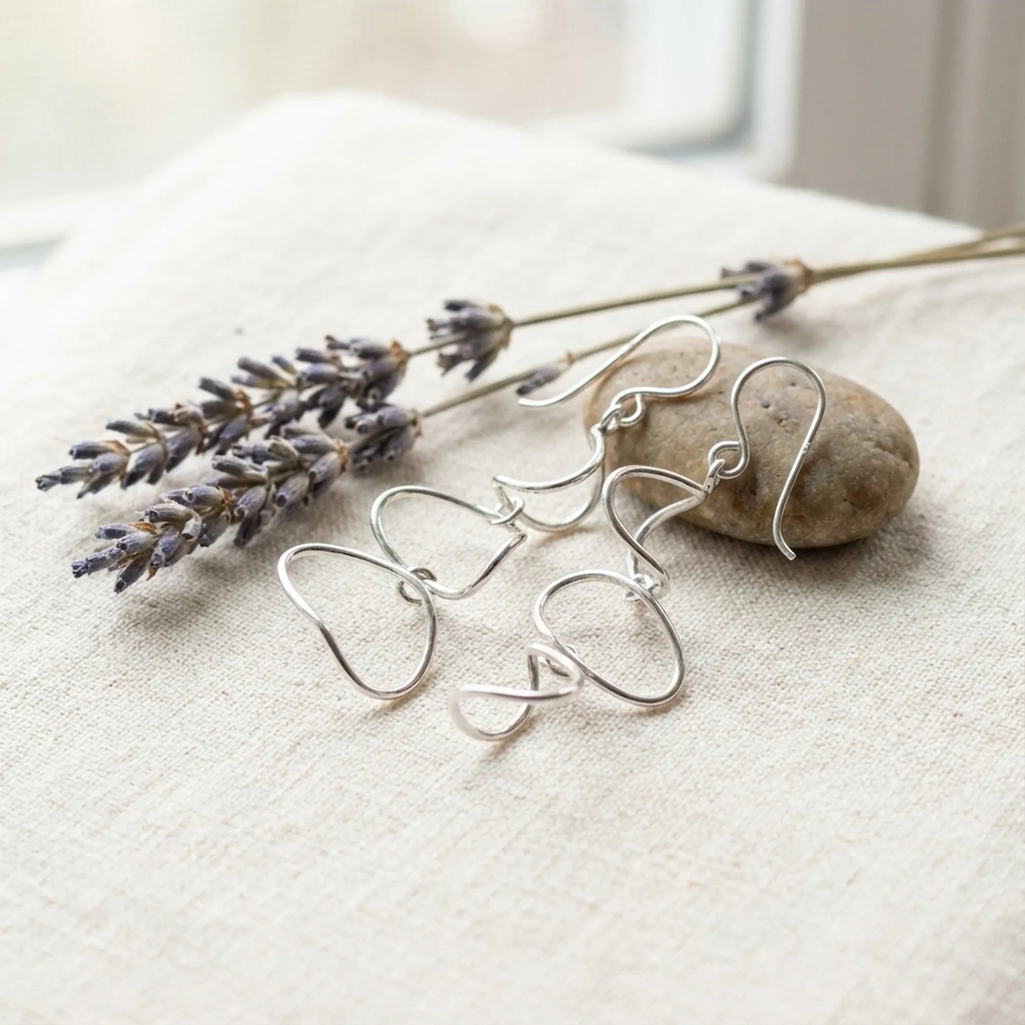 Silver cascading loop drop earrings on linen fabric with dried lavender stems and smooth pebble