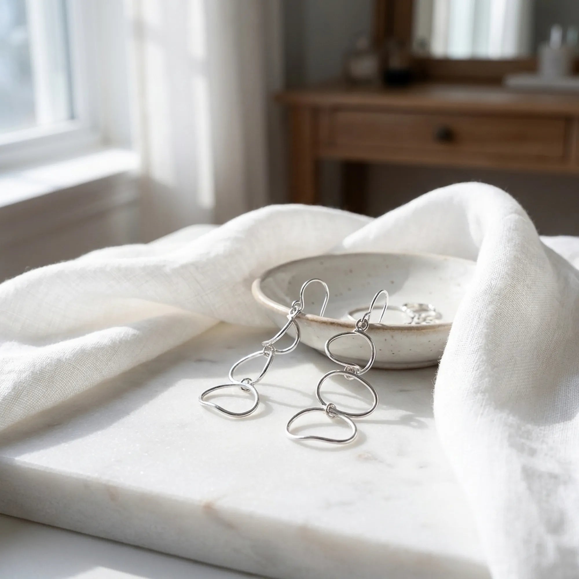 Abstract silver loop drop earrings on marble tray with ceramic dish and white linen fabric