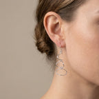 Model wearing silver abstract loop drop earrings on lobe, neutral taupe studio background at Luna Dura studio