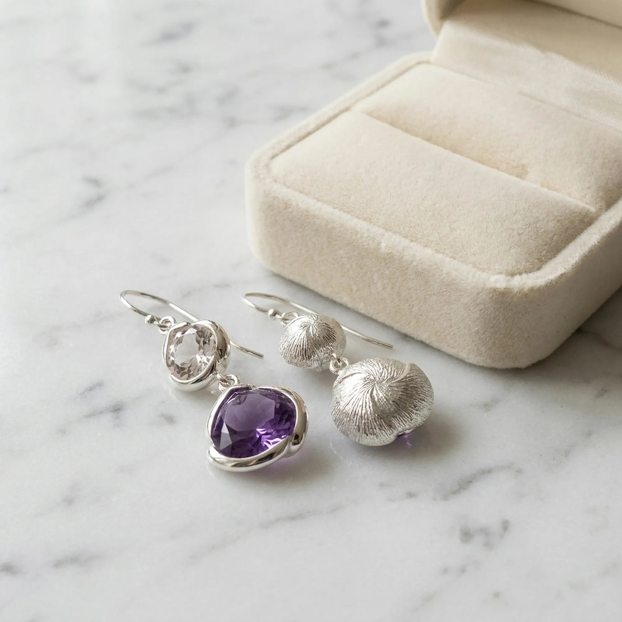 Amethyst lotus dangle earrings by a gift box, showing the stone front and engraved lotus reverse, Luna Dura Dubai.