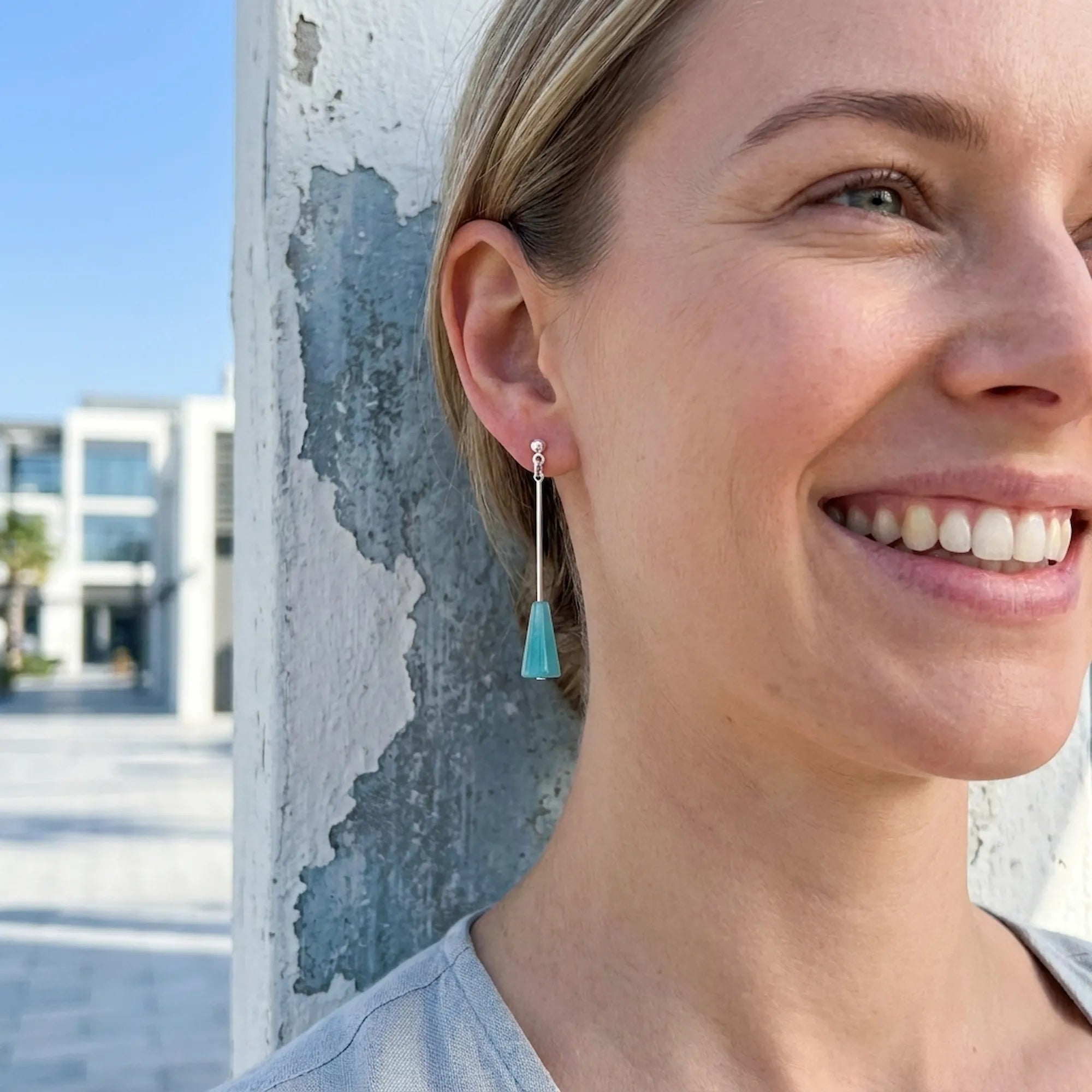 Woman wearing aqua blue lucite cone earrings outdoors in Dubai — minimalist geometric silver drop earrings GCC