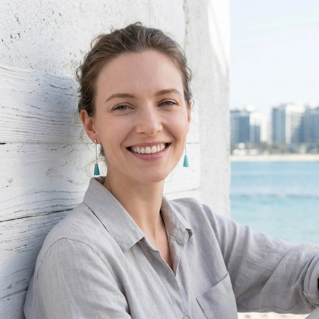 Model wearing aqua blue lucite cone drop earrings against Dubai waterfront skyline — 925 silver geometric drop earrings UAE