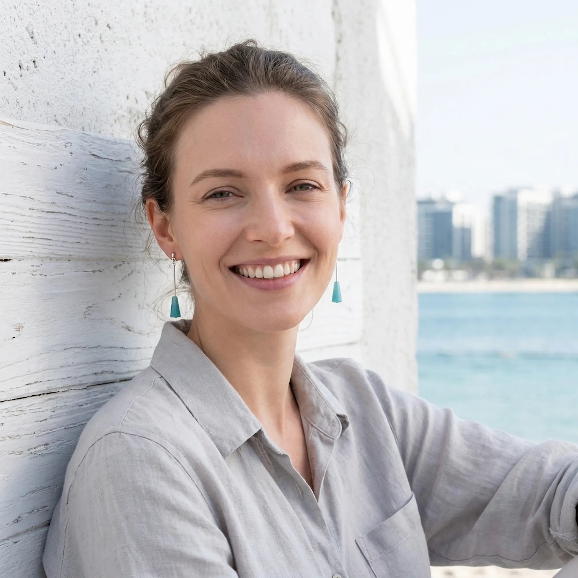 Model wearing aqua blue lucite cone drop earrings against Dubai waterfront skyline — 925 silver geometric drop earrings UAE