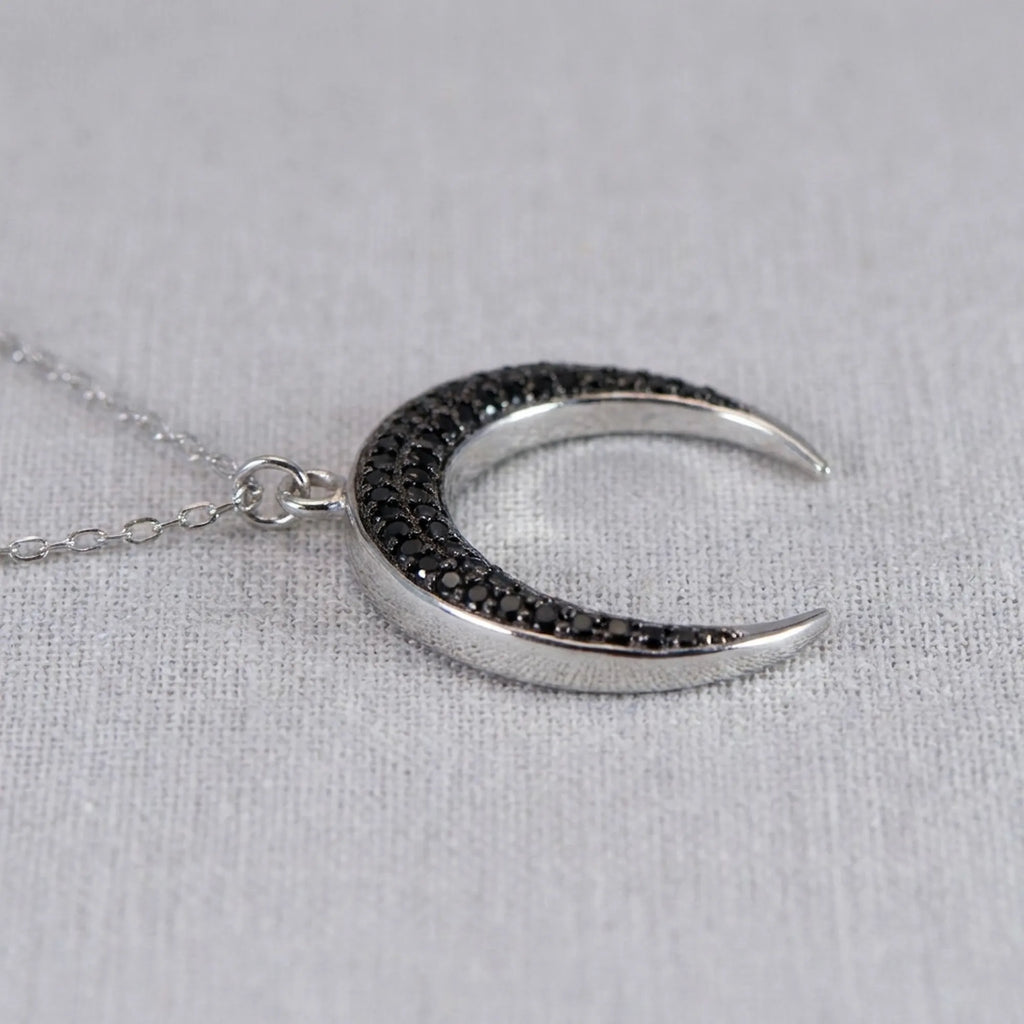 Side angle view of the Luna Dura sterling silver crescent moon pendant, showcasing the pave-set black zircon stones and high-polish finish