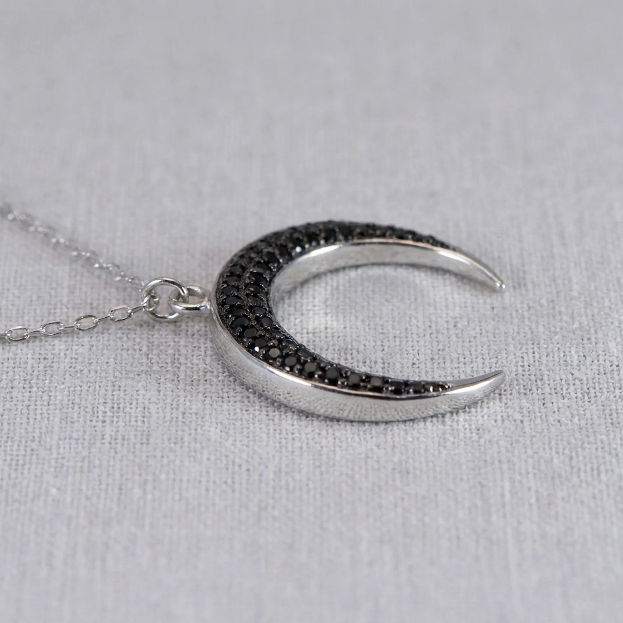 Side angle view of the Luna Dura sterling silver crescent moon pendant, showcasing the pave-set black zircon stones and high-polish finish