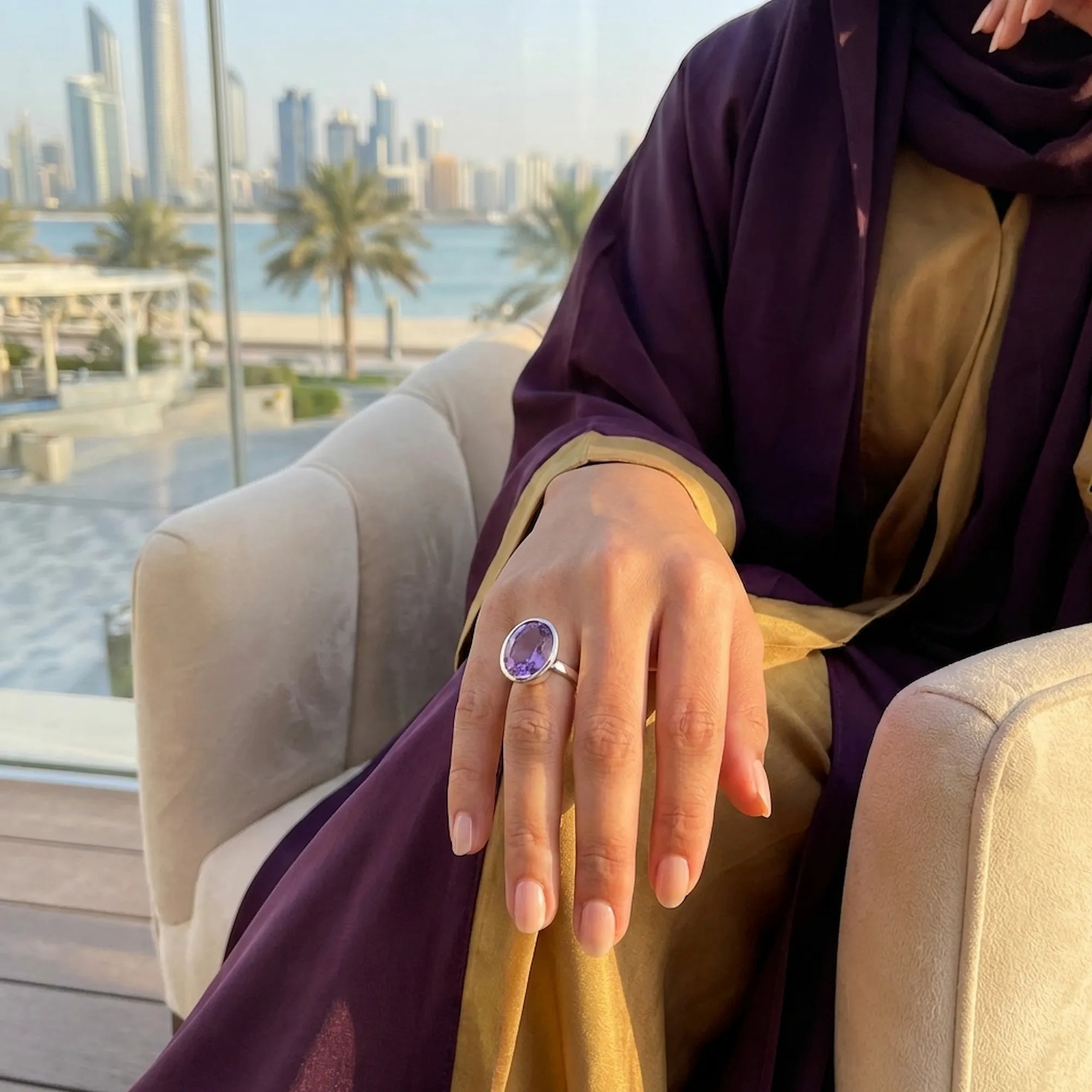 Woman in a purple and gold modest dress wearing the silver amethyst ring while seated with the Dubai skyline in the background.