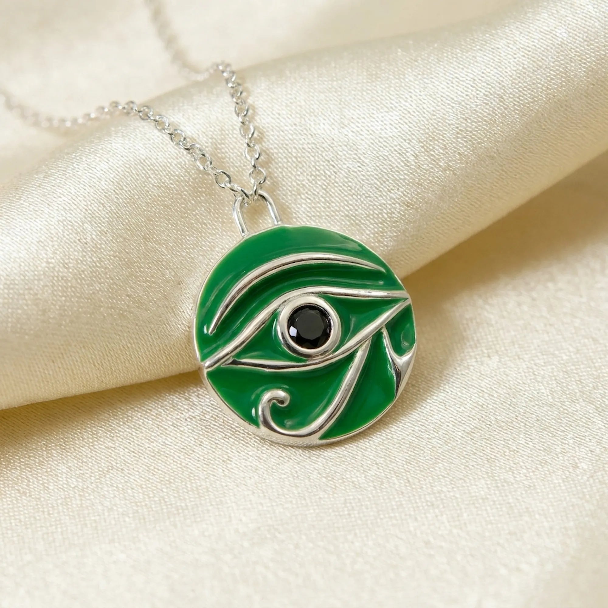 Green enamel and silver pendant necklace on a beige fabric background