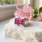 Emerald cut magenta quartz ring displayed on marble surface, blurred floral background, Luna Dura