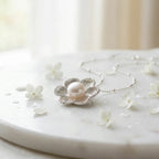 Silver magnolia pearl pendant on white marble surface with small white flowers, flatlay