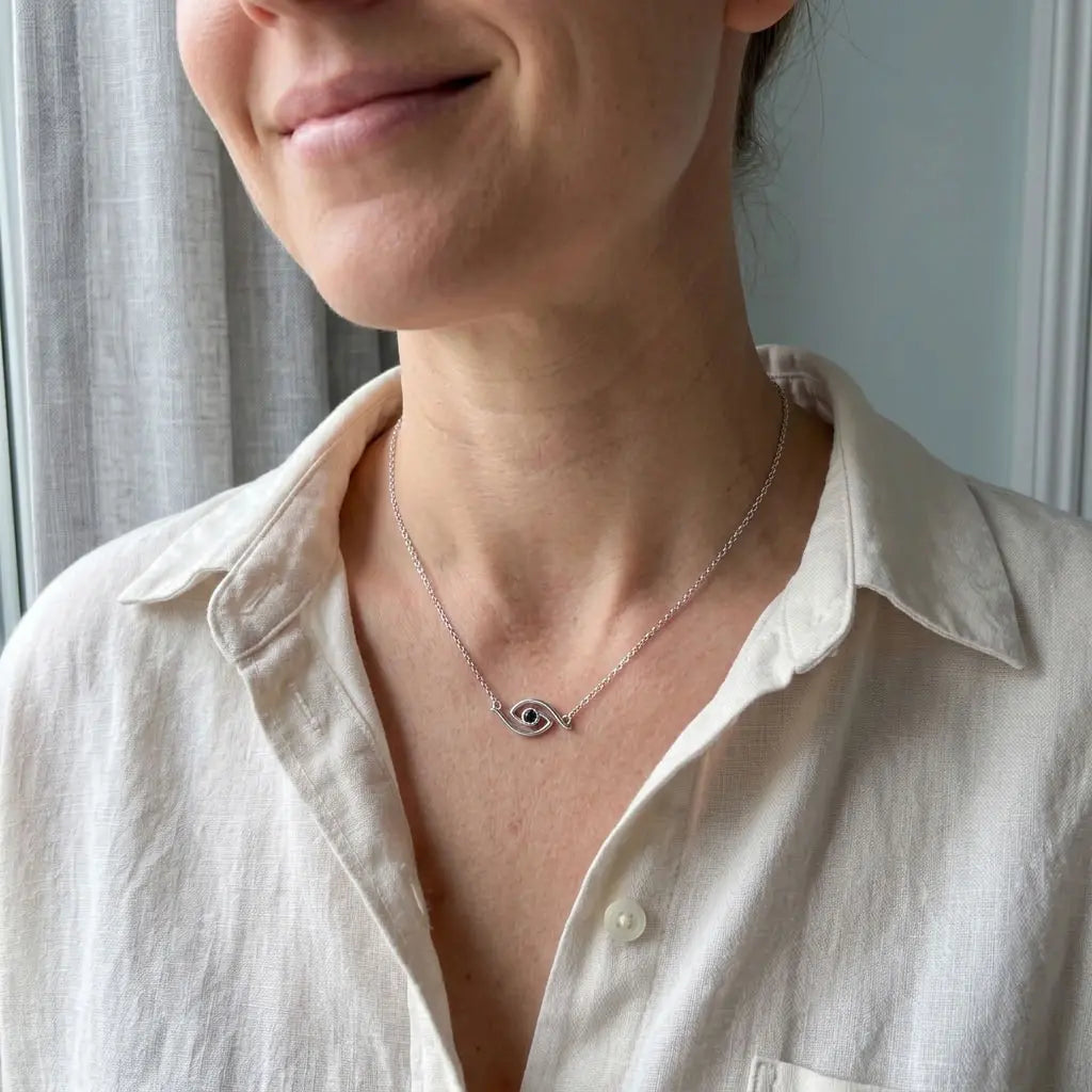 Modern blue CZ eye necklace with curved silver station motif worn with a light-coloured blouse.