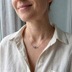 Modern blue CZ eye necklace with curved silver station motif worn with a light-coloured blouse.