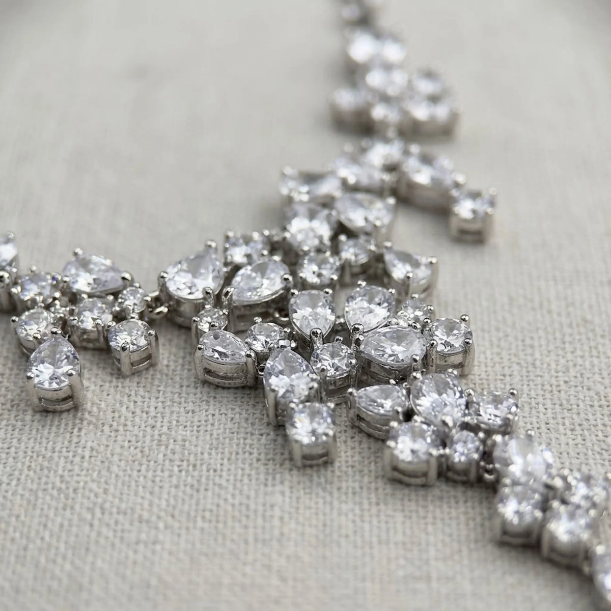 Macro view of a rhodium-plated cubic zirconia waterfall necklace showing mixed-cut stones on fabric in Dubai.