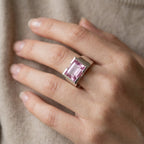 model Hand wearing a ring with a pink gemstone against a neutral background, Size reference  