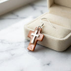 Warm brown winged oyster cross earring beside cream velvet jewelry box on marble — natural shell faith earrings Dubai