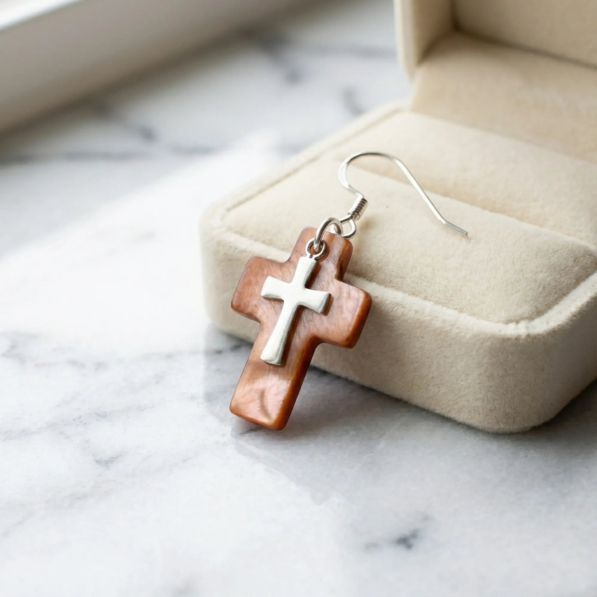 Warm brown winged oyster cross earring beside cream velvet jewelry box on marble — natural shell faith earrings Dubai