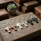  Three natural shell cross earring variants on rustic wood surface — white, black and brown Mother of Pearl with 925 silver crucifix Dubai