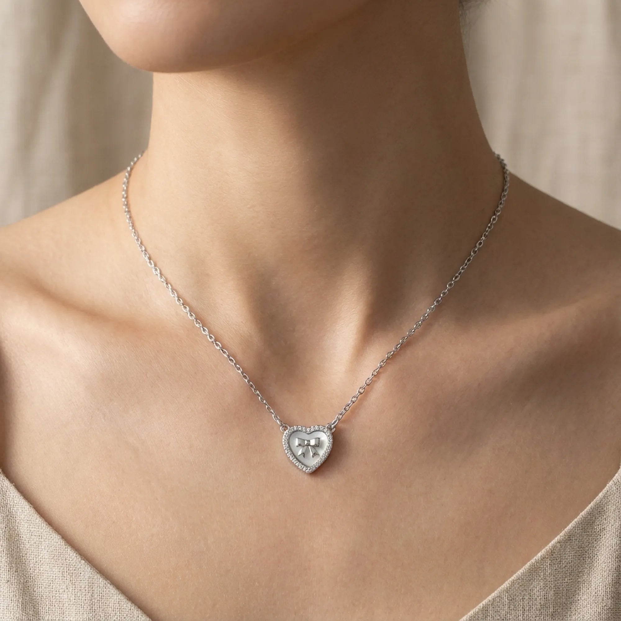 Mother of Pearl heart necklace worn at collarbone on model in linen top — CZ halo and bow detail visible, rhodium 925 silver Dubai