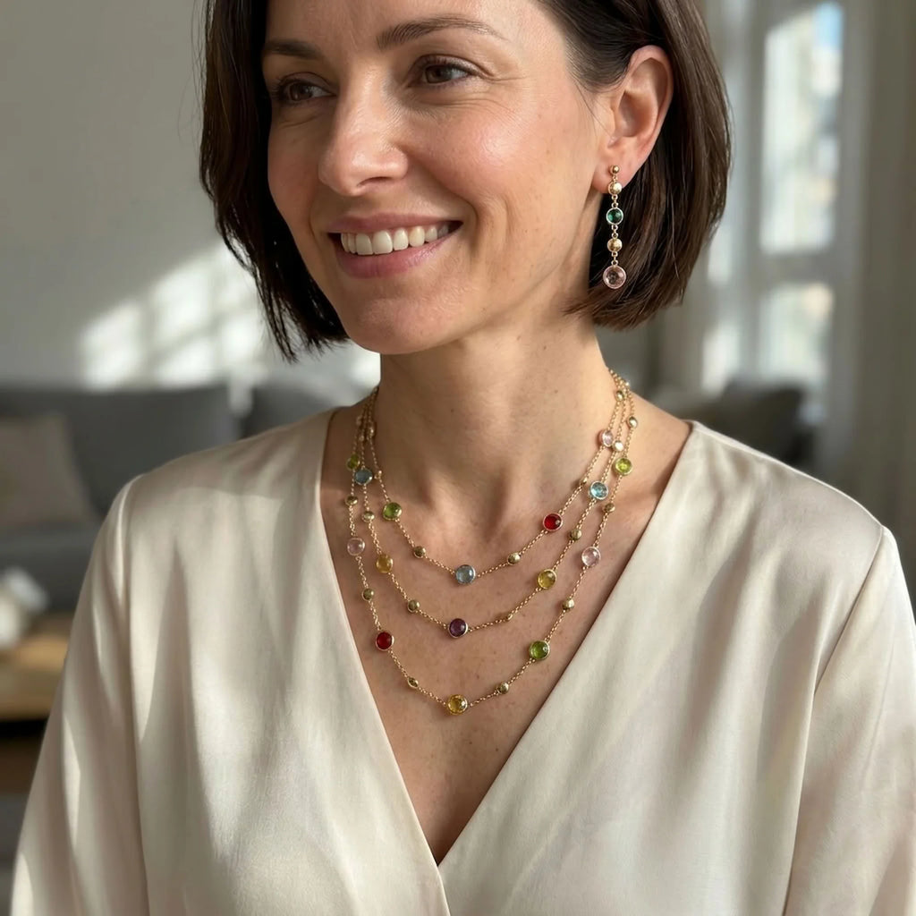 Woman wearing an 18k gold-plated multi-colour layered station necklace and matching linear drop earrings indoors in Dubai.