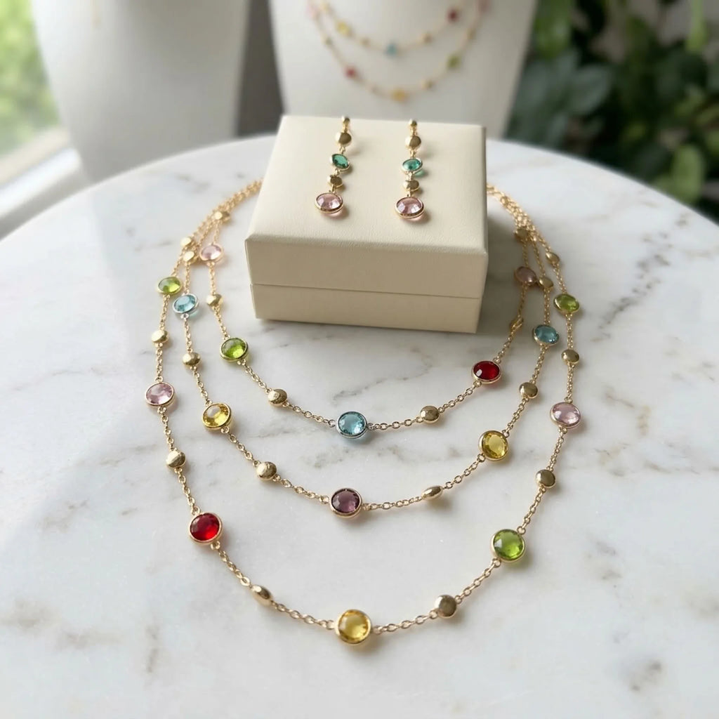 18k gold-plated multi-colour layered station necklace and earrings presented with a beige jewelry gift box on marble in Dubai.