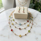 18k gold-plated multi-colour layered station necklace and earrings presented with a beige jewelry gift box on marble in Dubai.
