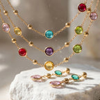 Close-up of 18k gold-plated layered necklace showing bezel-set multi-colour stones and golden disks resting on stone in Dubai.