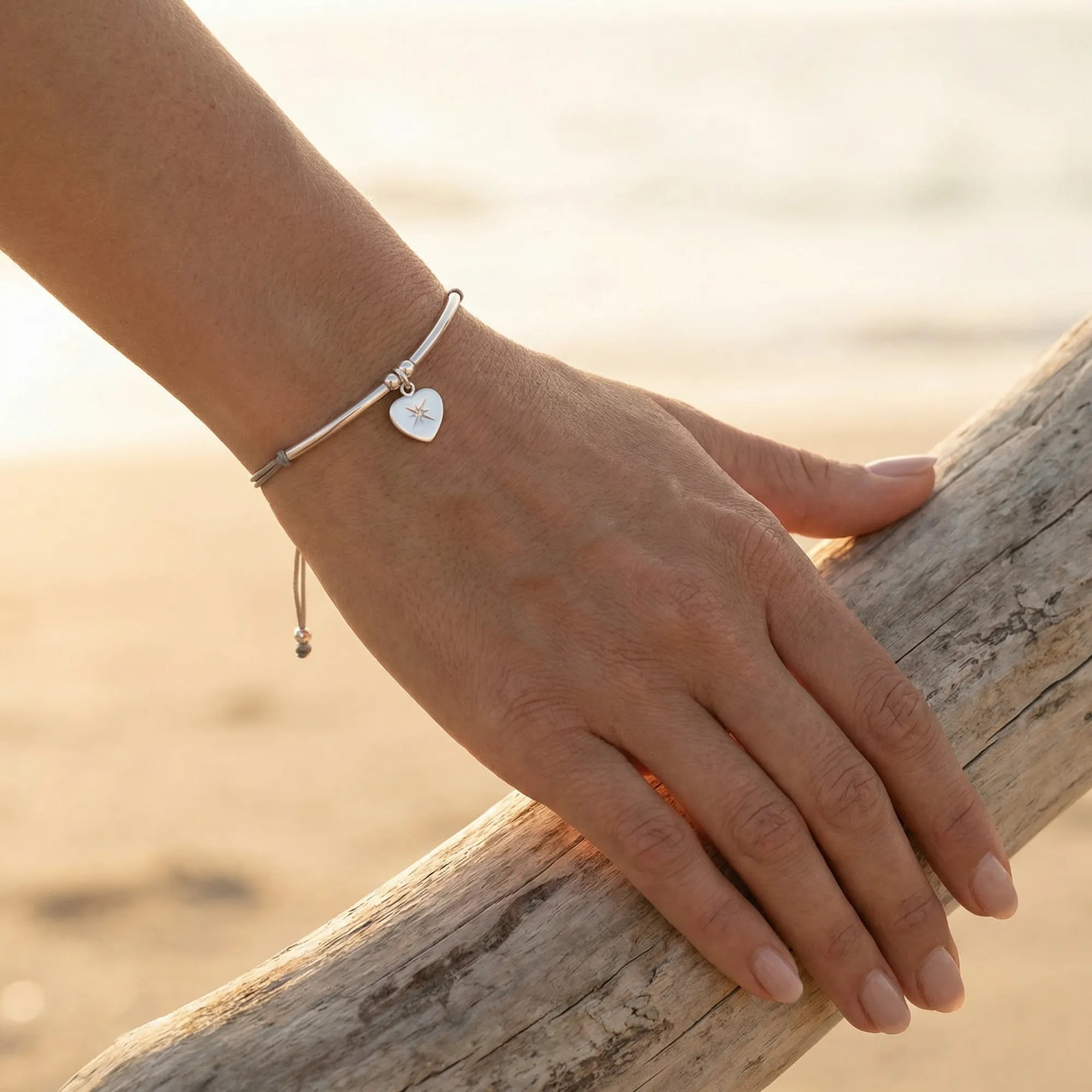 Silver North Star heart bracelet on the wrist at the Kite beach at golden hour, grey cord, Luna Dura Dubai